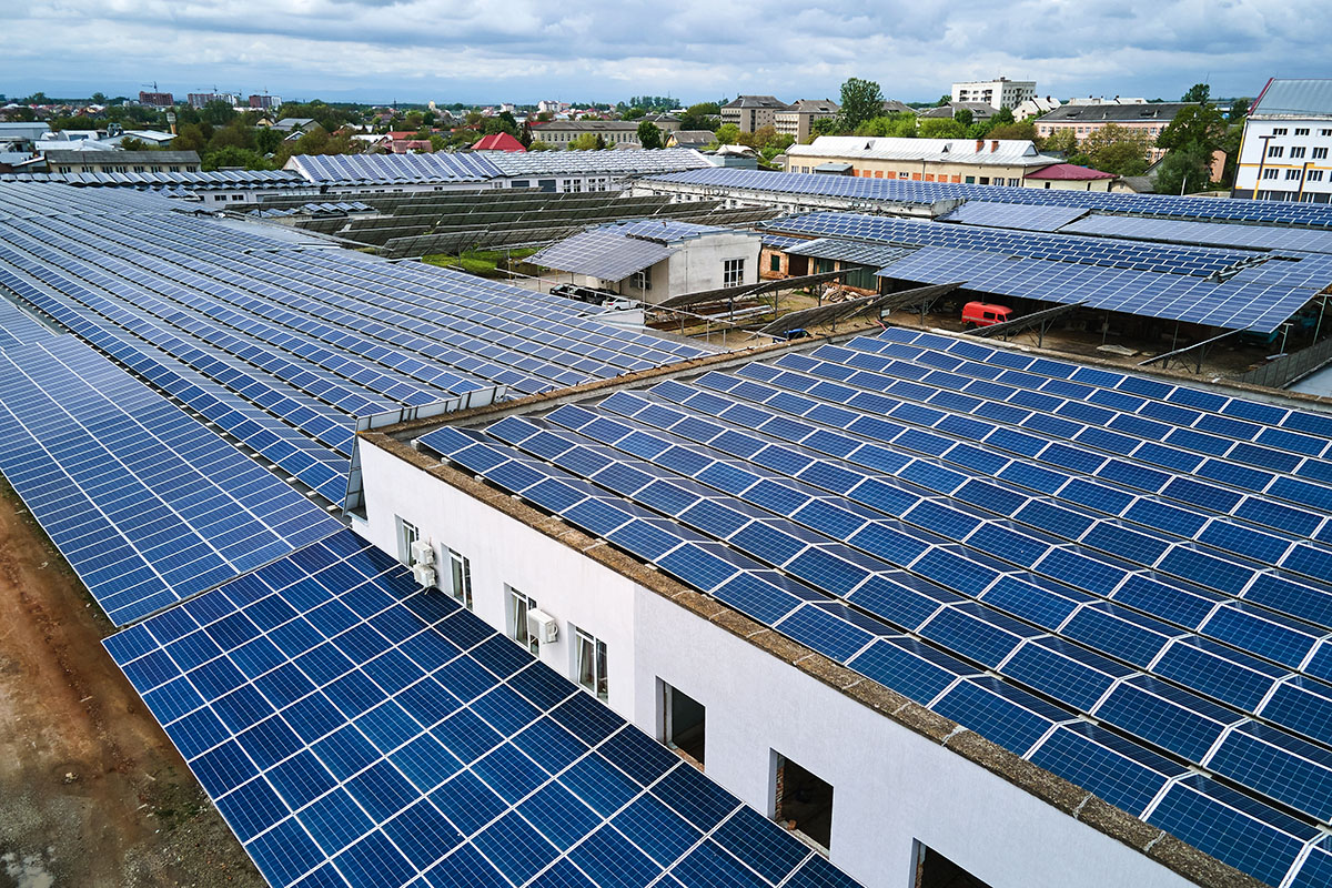 Aerial view of rows of blue solar panels covering the flat roofs of several industrial buildings