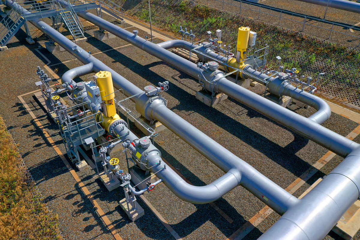 Silver gas pipelines with yellow valve actuators and instrument manifolds at an above-ground gas station, seen from above